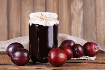 Tasty plum jam in jar and plums on wooden table close-up
