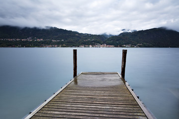 Fototapeta premium Tranquil scene of old wooden pier and misty Italian Alps mountai