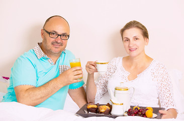 Middle aged couple having breakfast in bed of a house hotel 