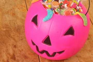 Pink plastic pumpkin filled with candy wooden table