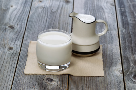 Full Glass of fresh milk and pourer on old wood