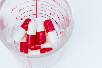white red capsules  in a cup of glass