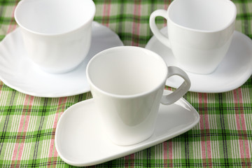 Fototapeta na wymiar Three white empty cups and saucers on green background.