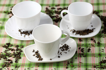 Fototapeta premium Three white empty cups and saucers with spilled green tea leaves