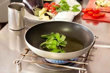 basil cooking inside pan with raw ingredients in the background