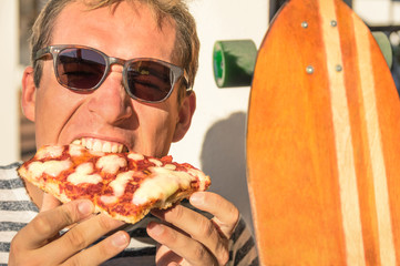 Young handsome hipster man eating a slice of pizza