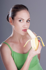 Charming woman eating a banana, over gray background.