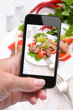 Hands taking photo vegetable salad with meat with smartphone