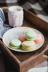 Hot cocoa in knitted cover and colorful macaroons on wooden tray
