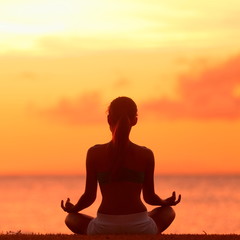 Naklejka premium Medytacja - medytując kobieta jogi o zachodzie słońca na plaży