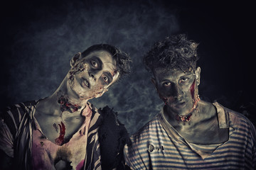 Two male zombies standing on black smoky background - obrazy, fototapety, plakaty