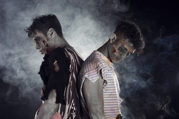 Two male zombies back to back on black smoky background