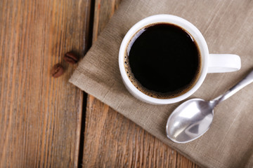 Cup of coffee and coffee beans on napkin on wooden background