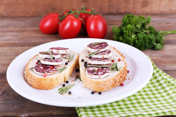 Sandwiches with salami on plate on napkin on wooden background