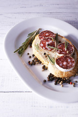Sandwich with salami on plate on wooden background