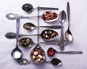 Tea in metal spoons on fabric background
