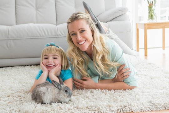 Smiling daughter and mother laying on the floor with rabbit