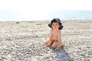 Funny boy in blue hat on the pebbles beach