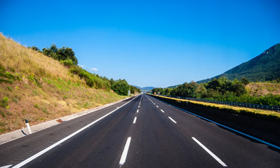 asphalt road through the green field and clouds on blue sky in s