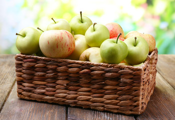 Ripe apples in basket on table on natural background