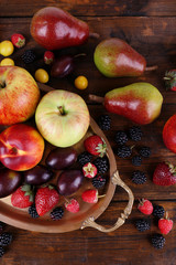 Naklejka na ściany i meble Different berries and fruits on tray on wooden table close-up