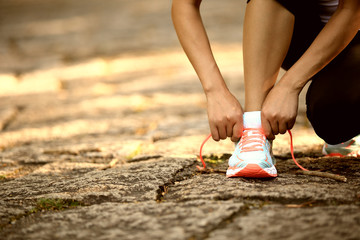 woman runner tying shoelace on stone trail