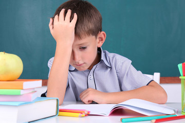 Schoolboy sitting in classroom on blackboard background