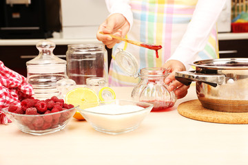 Woman cooking raspberry jam in kitchen