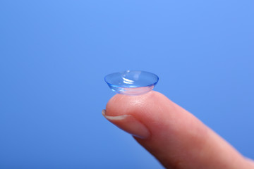 Contact lens on finger on blue background