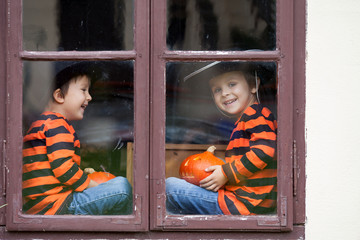 Two cute boys, sitting on a window with jack-o-lantern
