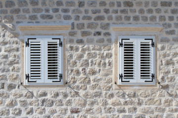 Two shuttered windows in the stone wall of the house