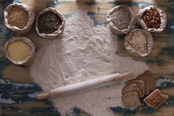 Grains, flour, bread and rolling pin on wooden table