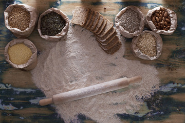 Grains, flour, bread and rolling pin on wooden table