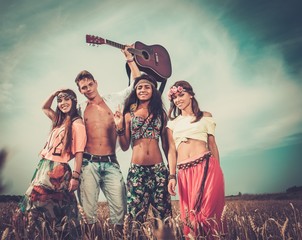 Multi-ethnic hippie friends with guitar in a wheat field