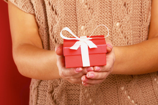 Female hand holding gift box isolated on red background