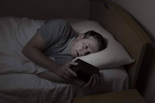 Mature Man checking time while trying to sleep
