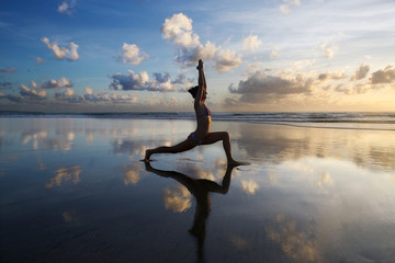 Young woman practicing yoga on the beach at sunset