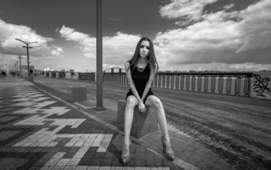 Fototapeta na wymiar Monochrome photo of sexy woman with long legs sitting on street