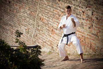 Man in karate stance with black belt in front of a brick wall