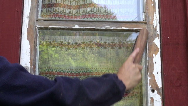 worker in farm scraping old paint from house window