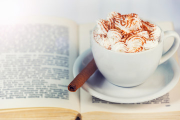 White cup of coffee, cream and cookie on book.
