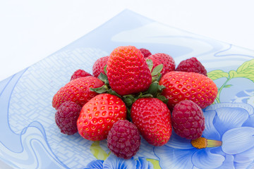 клубника выложенная в форме цветка с малиной на голубой тарелке