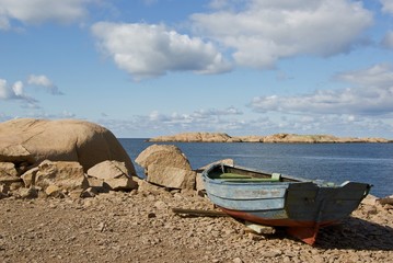 Fototapeta na wymiar Red granite boulders and an old rowing boat.