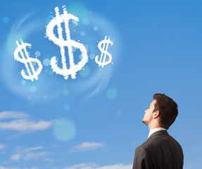 Businesman pointing at dollar sign clouds on blue sky