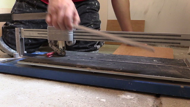 Tiler hands using tile cutter tool on floor. Left side slide