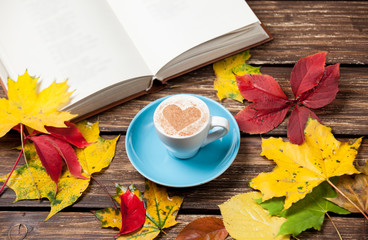 Autumn leafs, book and coffee cup on wooden table.