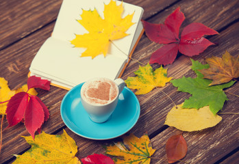 Autumn leafs, book and coffee cup on wooden table.