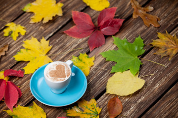 Autumn leafs and coffee cup on wooden table.