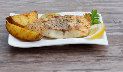 White fish with potato wedges on white plat, woodeen background