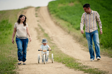 Family with little boy on tricycle in nature